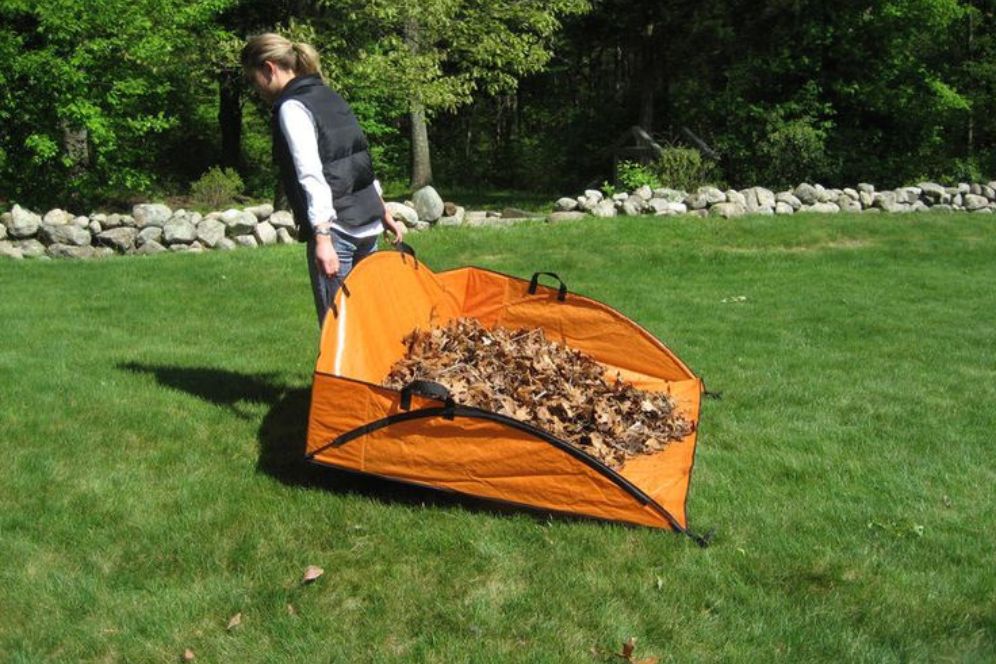 A woman is seen transporting a large orange bag stuffed with colorful leaves, indicating seasonal yard work.