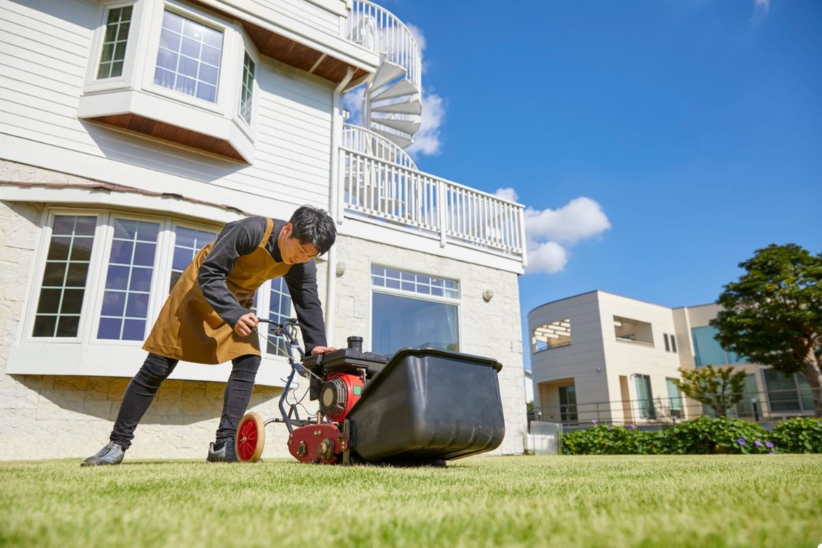 A man mowing the lawn in front of a well-maintained house on a sunny day.